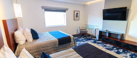 A hotel room with two beds, a desk, a chair, a TV, and a window.