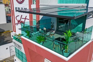 A modern outdoor seating area with glass railings, potted plants, and a clear view of the street. - Hotel Fray Select (Tepic)