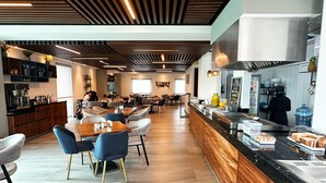 Een moderne eetruimte met houten tafels en stoelen, een keukentoog met etenswaren, en een bar.