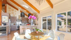 A modern kitchen with wooden beams, a dining area with glass tables, and large windows. - Trinity - Secluded Retreat - Pool, Hot Tub, Bocce (Glen Ellen)