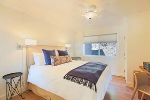 Un dormitorio con cama, lámparas de noche, ventilador de techo, ventana con vistas y escritorio con silla.