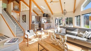 A spacious living area with a wooden staircase, a kitchen, and a large window providing natural light. - Trinity - Secluded Retreat - Pool, Hot Tub, Bocce (Glen Ellen)