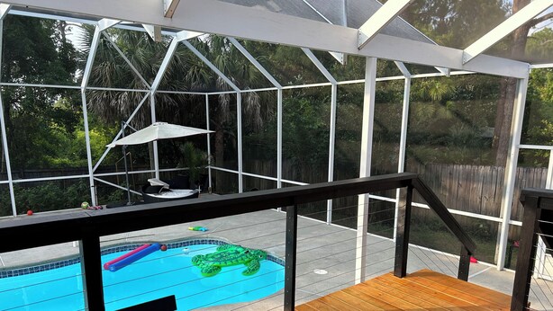 A pool area with a wooden deck, a glass-enclosed structure, and a green inflatable turtle float. - Casa Tranquilo    Heated Pool and Sauna (Gulf Breeze)