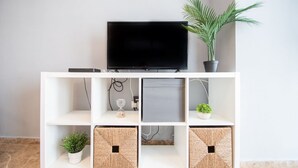 Un meuble de rangement blanc pour appareils multimédias, avec un téléviseur à écran plat, une plante en pot et des paniers décoratifs.