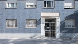Un immeuble à la façade en briques bleues, portant le numéro 9, avec une entrée en verre et des fenêtres dotées de grilles métalliques.