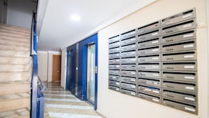 Un couloir avec un mur muni d’une fente métallique pour le courrier et une porte bleue.