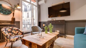 A modern living room with a wooden coffee table, a floral armchair, a sofa, and a TV mounted on the wall. - The Royal Elysée Suite (Paris)