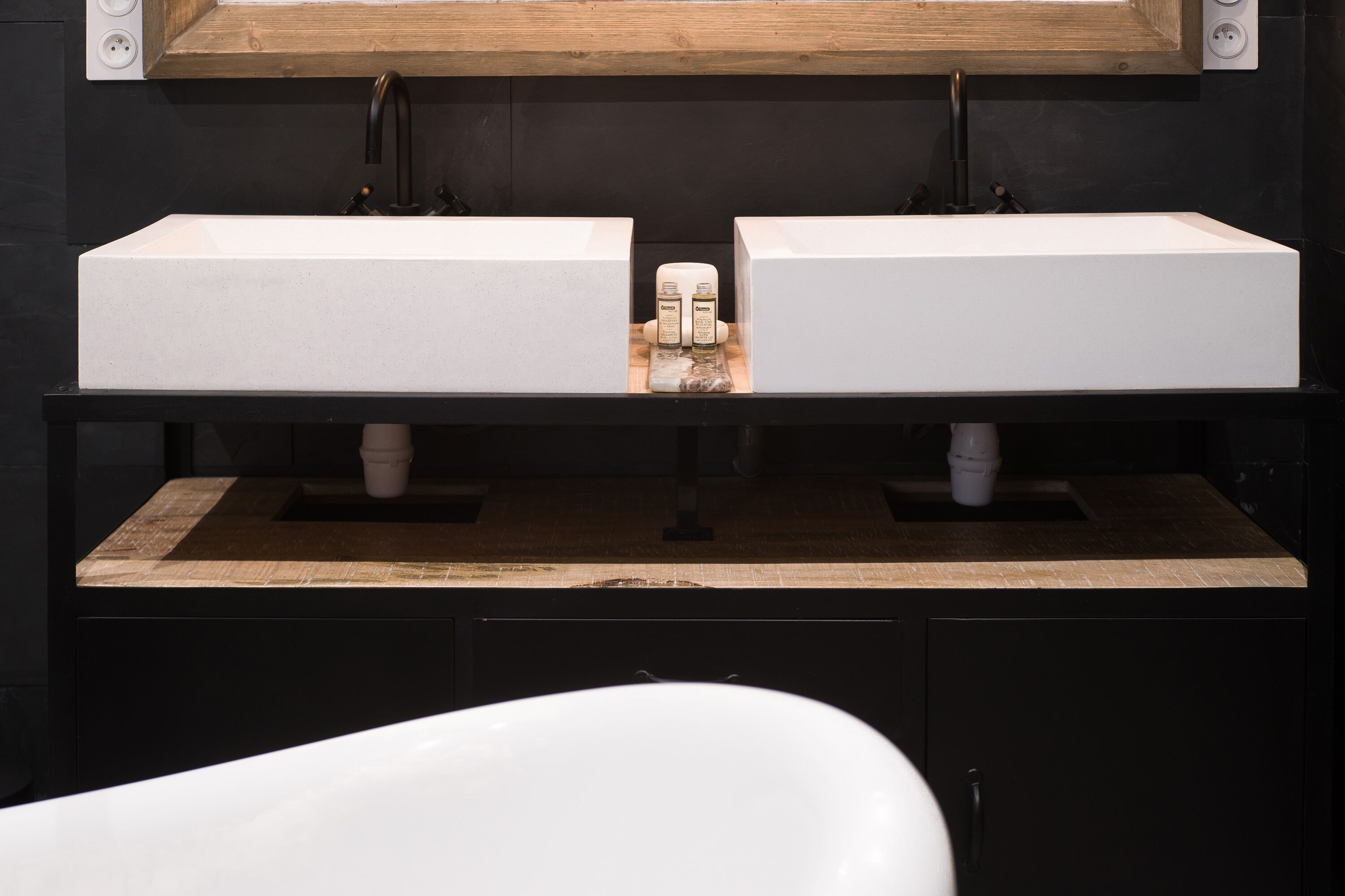 A modern bathroom with two white sinks, a wooden countertop, and a black cabinet below.