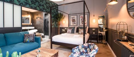 A modern bedroom with a four-poster bed, a blue sofa, a floral armchair, and a wooden coffee table.