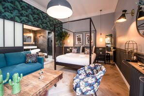 Een moderne slaapkamer met een hemelbed, een blauwe bank, een fauteuil met bloemenprint en een houten bijzettafeltje.