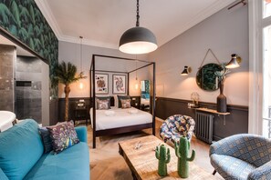 Een moderne slaapkamer met een hemelbed, een blauwe bank, een houten bijzettafeltje en een cactusdecoratie.