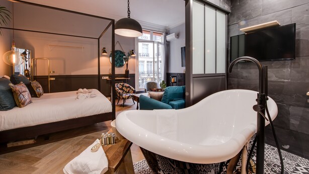 A modern bedroom with a large bed, a bathtub, and a TV mounted on the wall. - The Royal Elysée Suite (Paris)