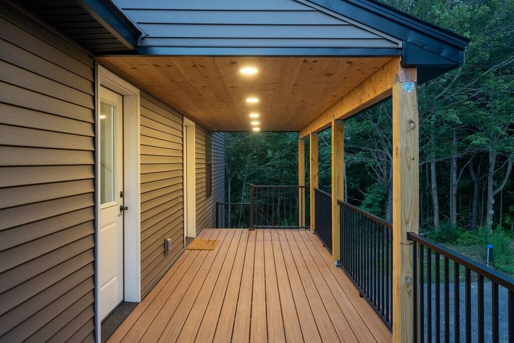Um deck de madeira com guarda-corpo, uma porta e área coberta com iluminação.