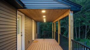 Um deck de madeira com guarda-corpo, uma porta e área coberta com iluminação.