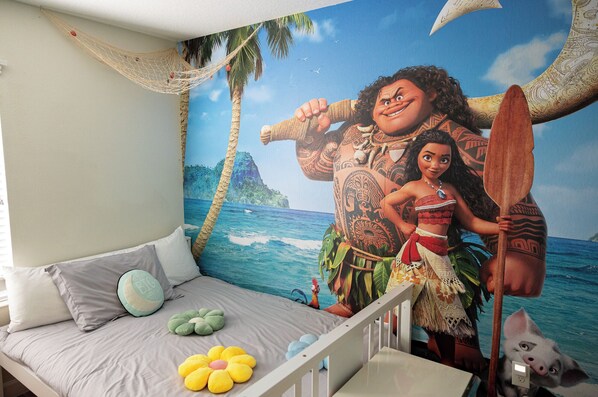 A bedroom with a bed, pillows, a wall mural, and a crib.