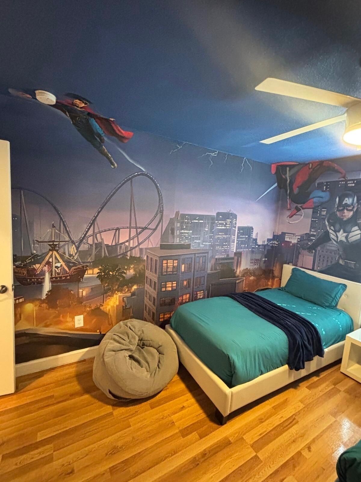 A bedroom with a cityscape mural, a bed, a bean bag, and a ceiling fan.