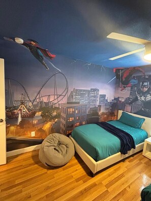A bedroom with a cityscape mural, a bed, a bean bag, and a ceiling fan.