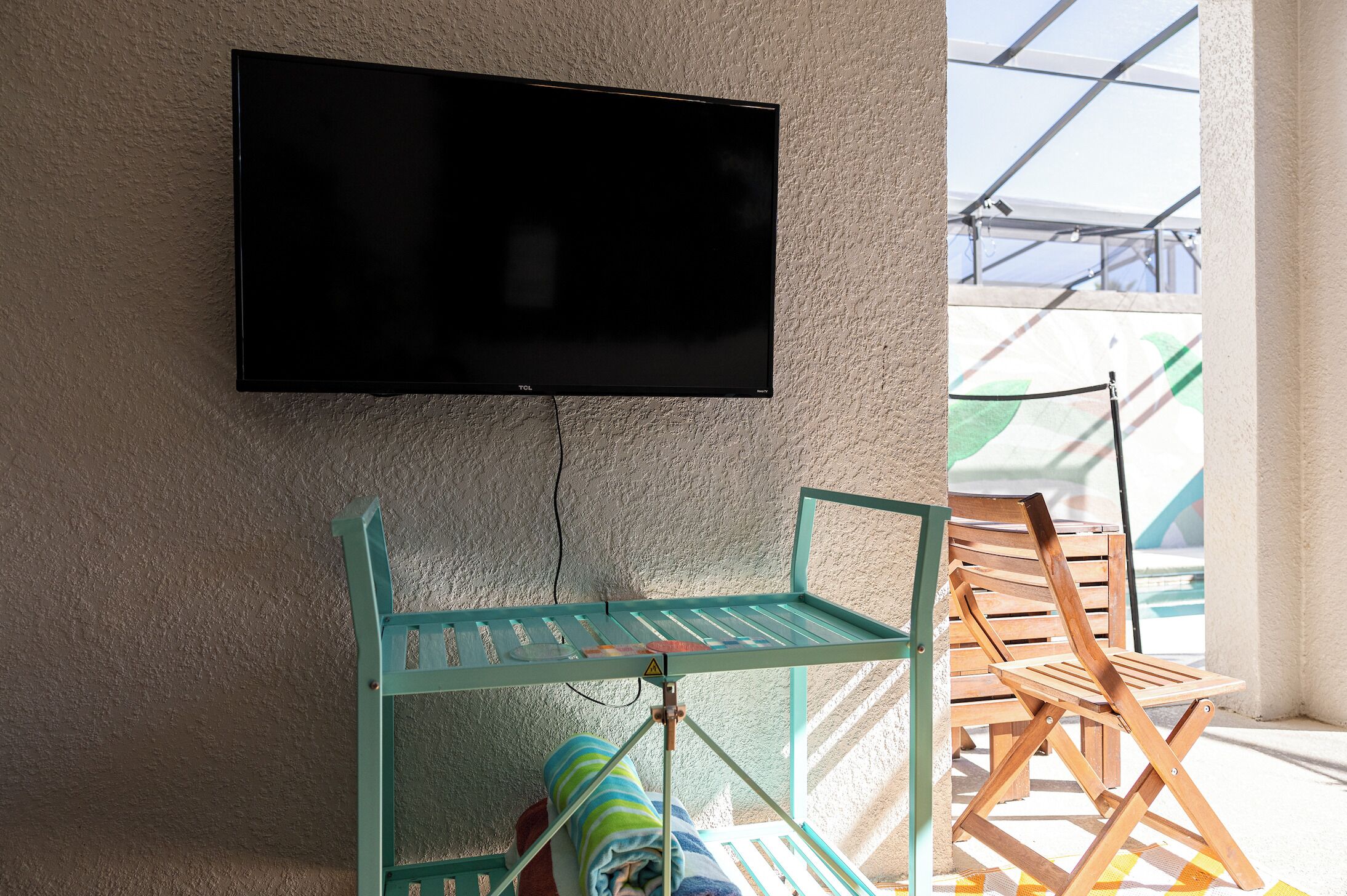 Une pièce équipée d’un téléviseur fixé au mur, d’un étendoir à linge en métal et d’une chaise en bois.