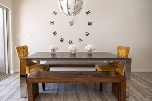 A dining area with a wooden table, two chairs, a bench, and a wall clock.