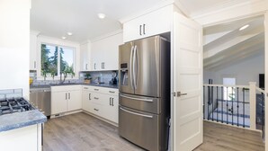 A modern kitchen with white cabinetry, a stainless steel refrigerator, and a gas stove. - Full House ➡️ Hut Tub (Aloha)