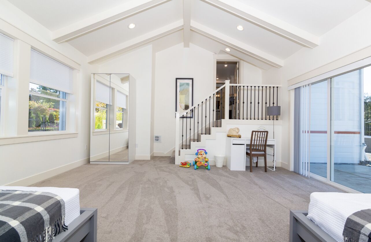 A spacious bedroom with a large window, a staircase leading to a balcony, and a desk area.