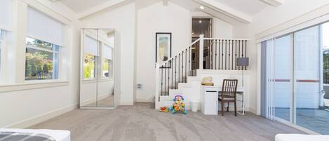 A spacious bedroom with a large window, a staircase leading to a balcony, and a desk area.
