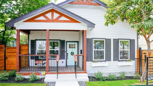 Une maison à deux étages avec un porche, une petite terrasse et une porte d’entrée.