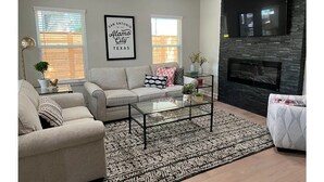 Un salon avec un canapé, une table basse et une cheminée. Un cadre décoratif est accroché au mur et un téléviseur est fixé au-dessus de la cheminée.