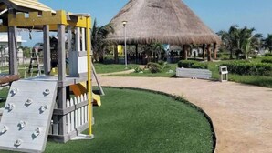 A playground with a slide and climbing wall, a thatched-roof structure, and a well-maintained lawn. - CASA KIM WHOLE HOUSE (Cancún)