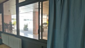 Ein Zimmer mit großem Fenster, Heizkörper und Blick auf einen Außenbereich mit Blumentöpfen und einem Gebäude im Hintergrund.