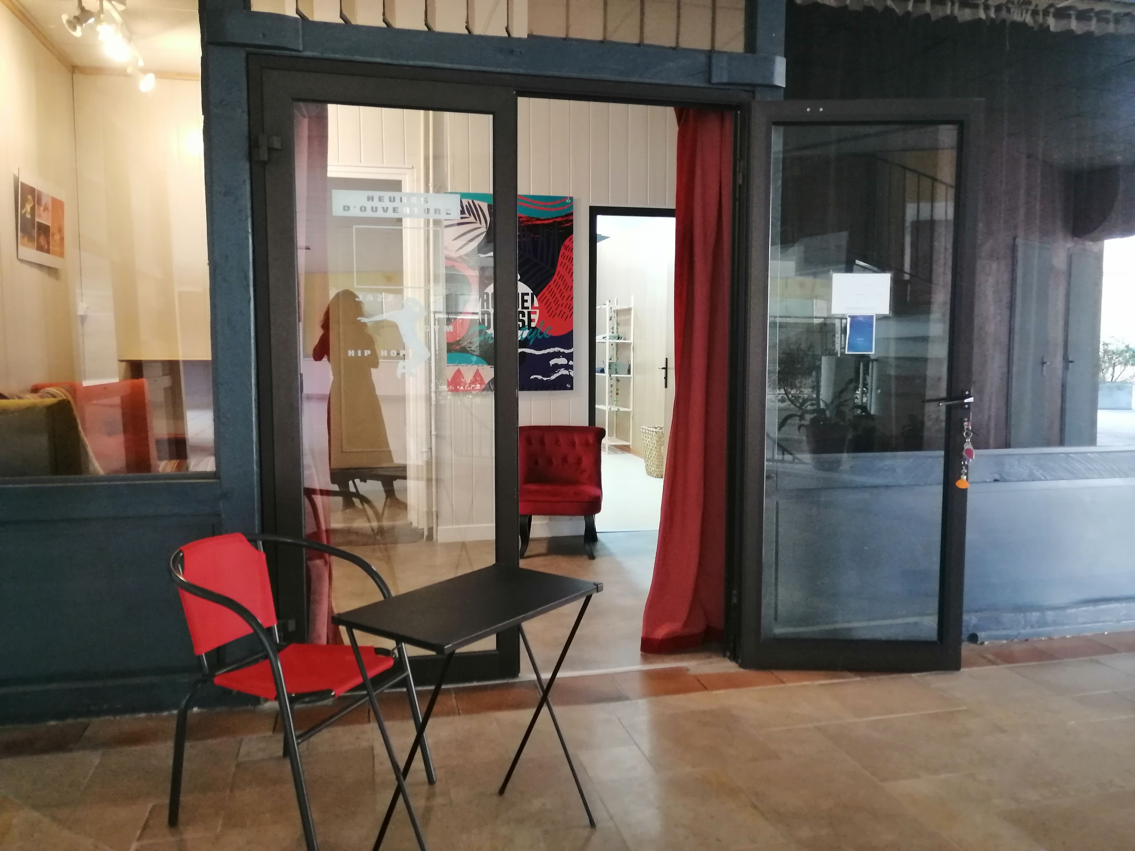 Ein Hotelzugang mit Glastür, einem roten Sessel, einem kleinen Tisch und einem roten Vorhang.