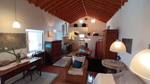 A cozy, well-lit living room with a dining area, wooden ceiling, and a kitchen in the background. - Charming Cottage in the Heart of the Village, Near Barroque Church (Castelo Branco, Horta, Faial)