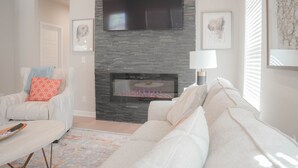 A living room with a fireplace, a flat-screen TV mounted above it, and a sofa.