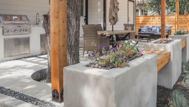 A covered patio area with a grill, seating, and planters.