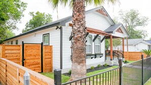 A single-story house with a covered porch, wooden fence, and a palm tree.