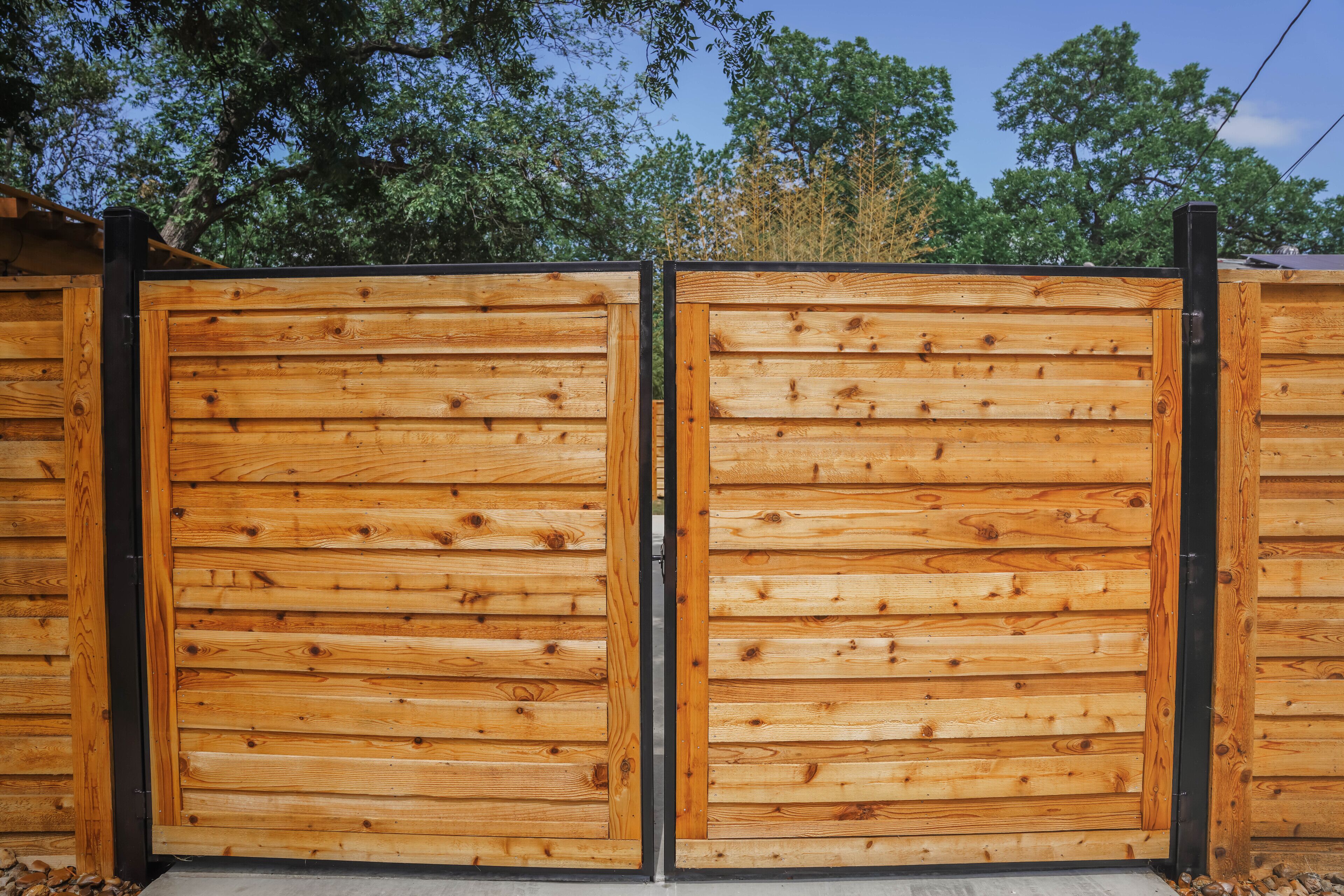 A wooden gate with a metal frame, set against a backdrop of trees.