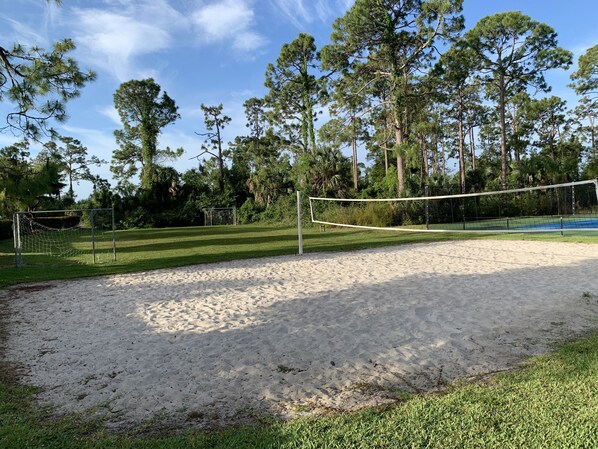 A sandy beach volleyball court with a net, surrounded by trees and a clear sky.