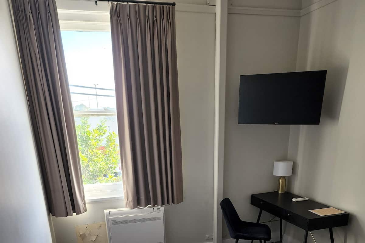 Habitación de hotel con cama, escritorio, silla, televisor y ventana con cortinas.