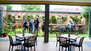 An outdoor patio area with tables and chairs, a wooden pergola, and hanging planters. - The Young Street Hotel (Carrington)