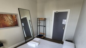 A hotel room with a neatly made bed, a small bedside table, a mirror, and a door. - The Young Street Hotel (Carrington)