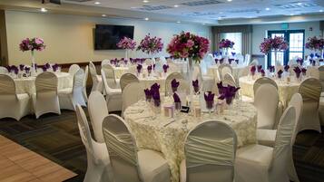 A banquet hall with round tables, white chairs, and floral centerpieces.