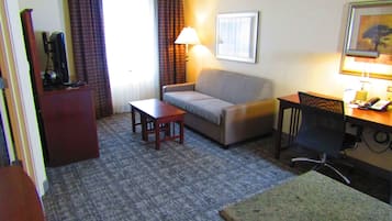 Habitación de hotel con sofá, una mesita, escritorio con silla, lámpara y televisión.