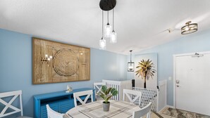 Un comedor con una mesa redonda, sillas blancas, una consola azul y una obra de arte colgada en la pared.