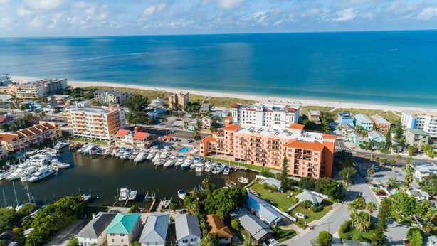 An aerial view of a coastal town with a marina, beachfront, and various buildings including hotels.