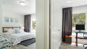 A bedroom with a bed, bedside table, lamp, and a desk with a computer.