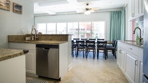 A kitchen with a dishwasher, granite countertops, and a dining area with chairs and a table.