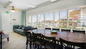 A spacious room with a large dining table, comfortable seating, a ceiling fan, and a view of a marina through large windows.