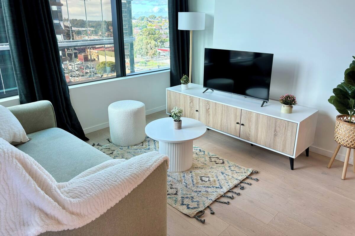 En moderne stue med sofa, skammel, fjernsyn og planter.