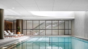 Una piscina interior con paredes de vidrio transparente, una escalera y sillones de descanso.