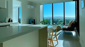Una cocina moderna con una isla grande, un comedor con sillas y un sofá. Hay un ventanal que ofrece vistas de la ciudad.